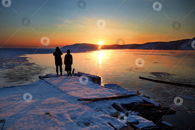 Скачать Закат солнца на весеннем озере Байкал. Молодая пара любуется закатом над озером фотосток Ozero