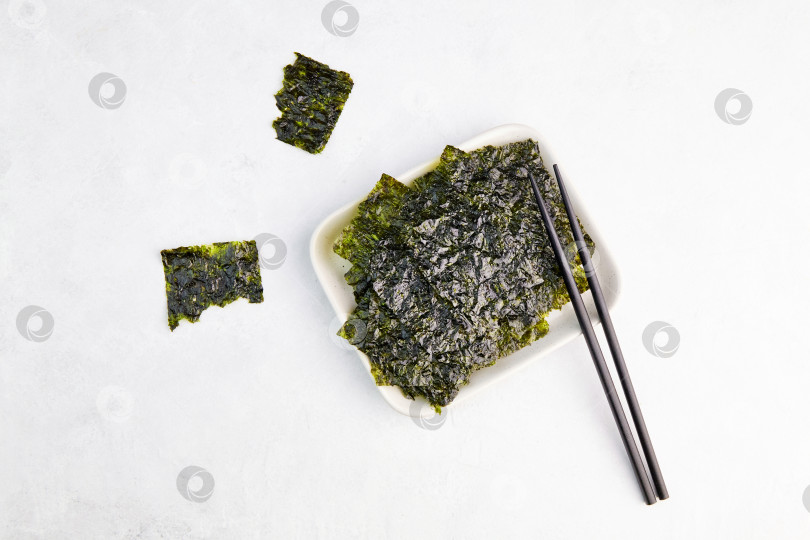 Скачать Хрустящие водоросли нори выложите на тарелку палочками для еды. Полезная закуска. Традиционные японские сухие листы из морских водорослей фотосток Ozero