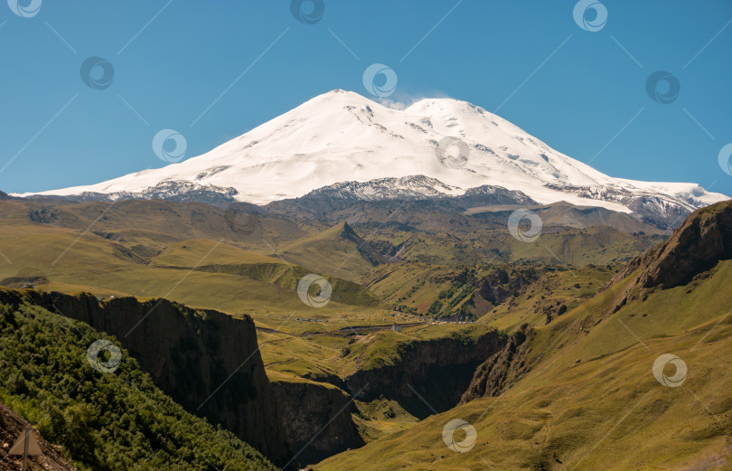 Скачать Россия, Кавказские горы. Вид на заснеженную вершину Эльбруса и зеленую долину. фотосток Ozero