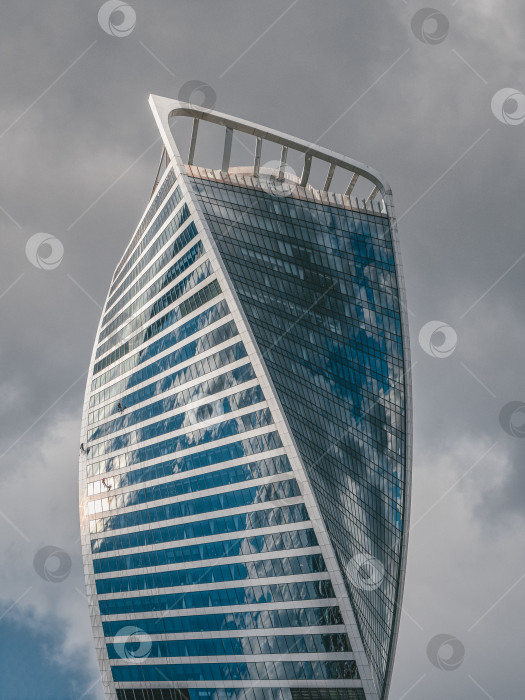 Скачать Современное высотное здание из стекла и бетона с маленькими силуэтами высотных рабочих на стене фотосток Ozero