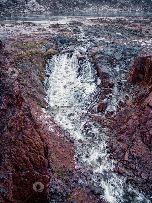 Скачать Замерзший водопад, падающий со скалы. Атмосферный минималистский арктический пейзаж с висячим ледником на вершине скалистой горы. фотосток Ozero
