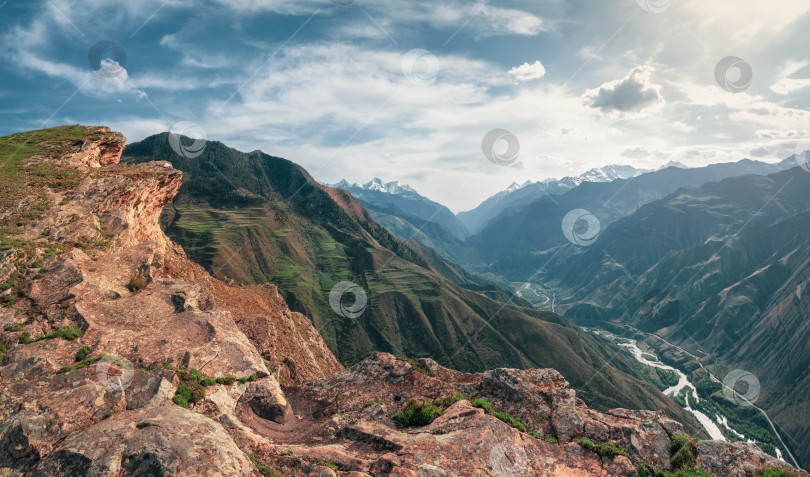Скачать Красочный летний пейзаж с силуэтами больших скалистых гор и эпическим глубоким ущельем с рекой.Край скалистого обрыва с прекрасным панорамным видом на ущелье. фотосток Ozero