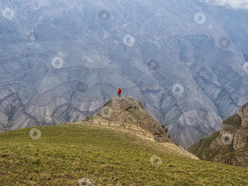 Скачать Маленький силуэт женщины с рюкзаком стоит спиной к обрыву. Уединение в горах, концепция одиночного путешествия. фотосток Ozero
