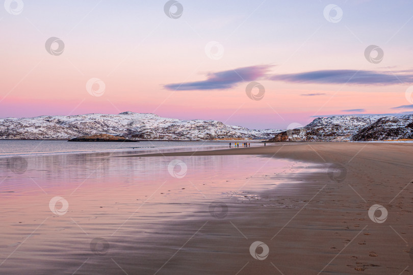 Скачать Группа путешественников вдалеке на пляже. Прекрасный розовый закат над Северным Ледовитым океаном. Полуостров с заснеженными холмами на горизонте. Морской минималистичный пейзаж. фотосток Ozero