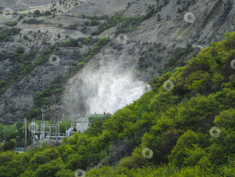 Скачать Сброс воды на гидроэлектростанциях. Гидроэлектростанция в горах, покрытых пышным зеленым лесом фотосток Ozero