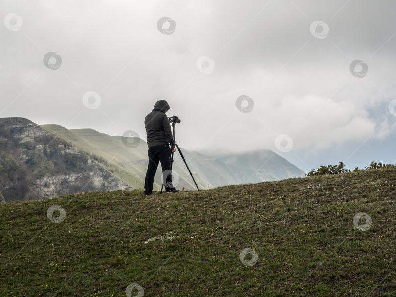 Скачать Фотограф снимает пейзаж со штатива, стоя на краю обрыва в сложных погодных условиях. фотосток Ozero