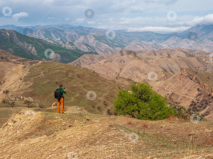 Скачать Турист мужского пола с рюкзаком на смартфоне фотографирует красивый горный пейзаж. фотосток Ozero