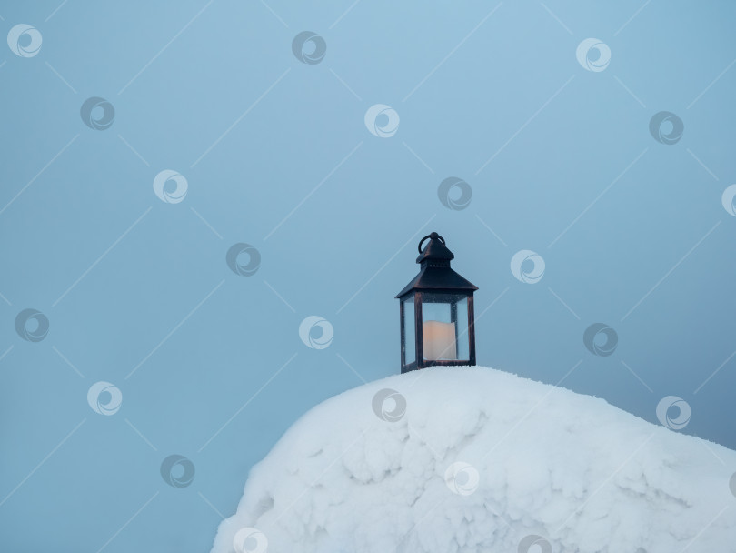 Скачать Старый фонарь со свечой стоит на вечернем снегу морозной зимой. фотосток Ozero