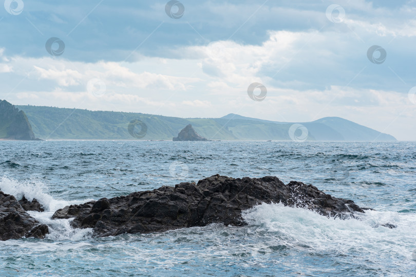 Скачать морской пейзаж с далеким лесистым берегом на заднем плане и скалами в прибое на переднем плане, пейзаж острова Кунашир фотосток Ozero