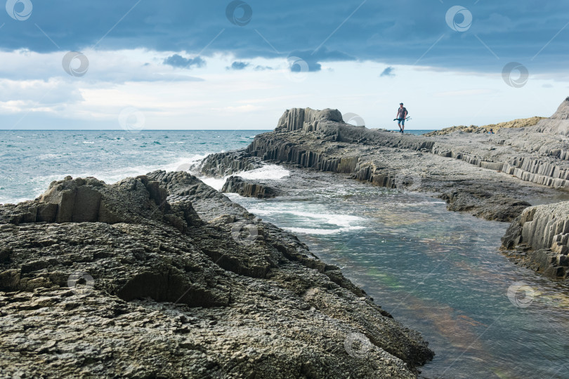 Скачать прибрежный морской пейзаж с красивыми столбчатыми базальтовыми скалами во время отлива, рыбак виден вдалеке в размытом виде фотосток Ozero