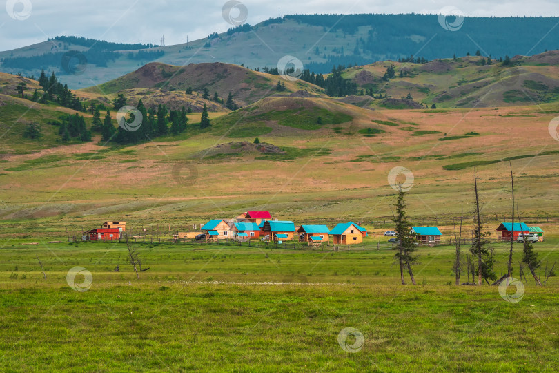 Скачать Современная сельская местность в высокогорье. Коллективный кемпинг вдалеке, туристический комплекс, деревянные гостевые домики на фоне зеленых холмов. Усадьба в степи. фотосток Ozero