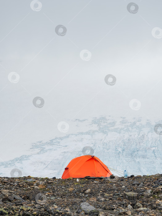 Скачать Оранжевая палатка на утесе в леднике. Экстремальный ночлег в горах. Покой и расслабление на природе. Вертикальный вид. фотосток Ozero