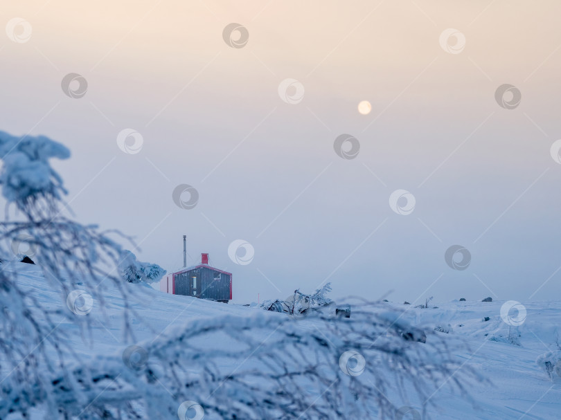 Скачать Одинокое красное бунгало на заснеженном морозном холме под темным вечерним небом фотосток Ozero