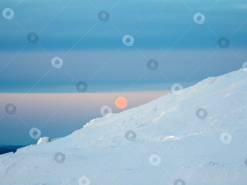 Скачать Красная полная холодная луна над заснеженным склоном. Зимний полярный пейзаж. Холодная зимняя погода. Суровый северный климат. Минималистичный вид. фотосток Ozero