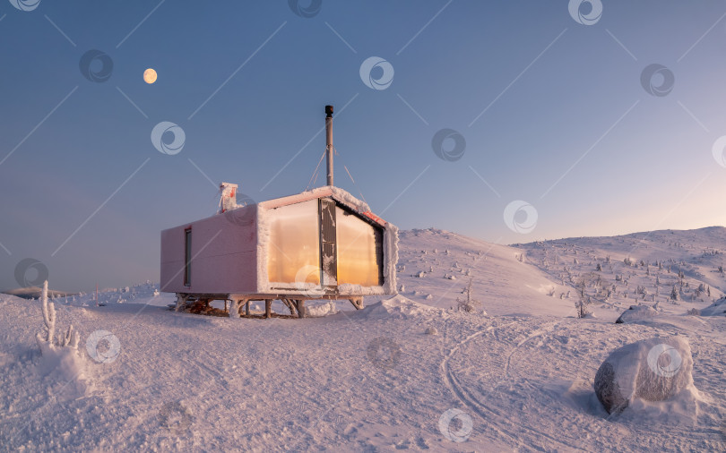 Скачать Одинокий красный дом на заснеженном морозном холме под рассветным небом с полной луной. Панорамный минималистский фон с изображением одинокой красной хижины зимой. Зимние каникулы, уют в морозную ночь. фотосток Ozero