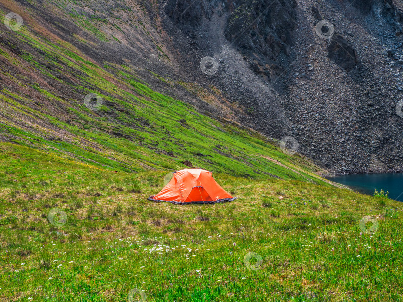 Скачать Живописный альпийский пейзаж с оранжевой палаткой рядом с красивой зеленой горной долиной Хайленд. Солнечный высокогорный пейзаж с оранжевой палаткой. Концепция путешествия. фотосток Ozero