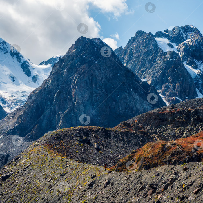 Скачать Заснеженный высокогорный альпийский пейзаж с заснеженной горной вершиной и острыми скалами под облачным голубым небом. фотосток Ozero