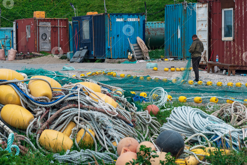 Скачать рыбак проверяет и ремонтирует промышленные рыболовные сети на берегу на рыболовной базе фотосток Ozero