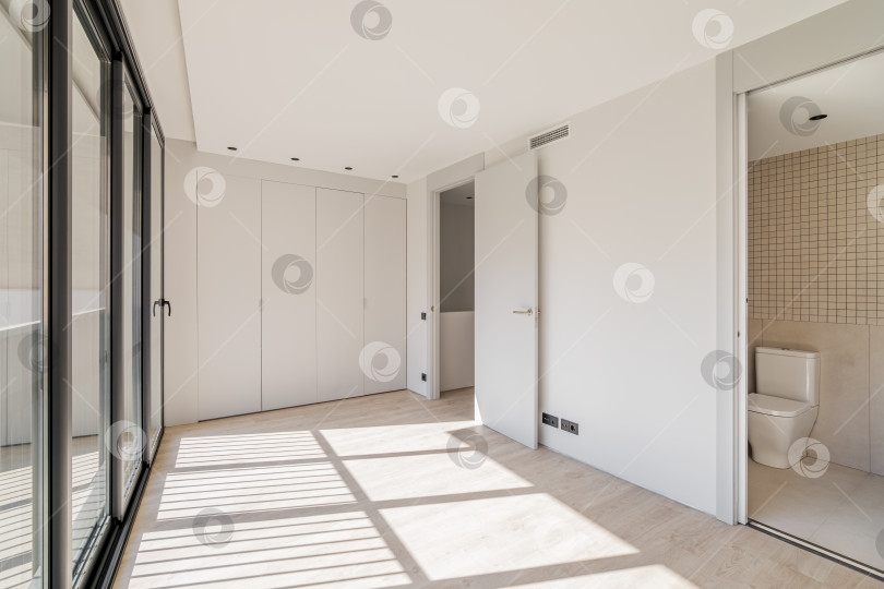 Скачать Пустая комната со встроенным шкафом во всю стену. С отдельными помещениями для туалета и прачечной. Комната с большими окнами во всю стену, через которые яркое солнце освещает просторную комнату. фотосток Ozero