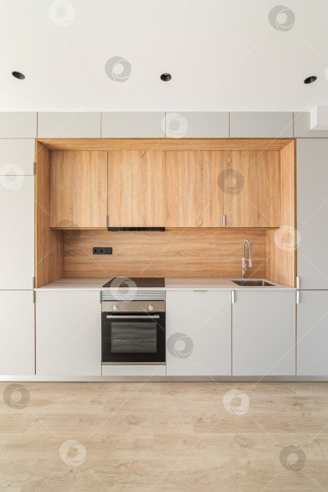 Скачать Простая пустая модульная кухонная зона в современной квартире. Мебельный минимализм с большим количеством шкафчиков, духовки и плиты для приготовления вкусной еды. фотосток Ozero