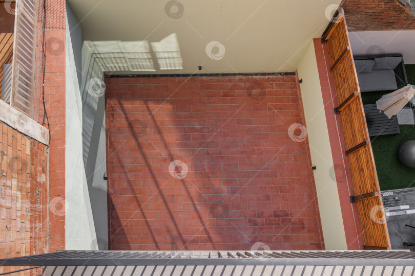 Скачать Вид сверху на закрытый частный двор с полом из красного кирпича, окруженный высокими стенами. Зона для отдыха на свежем воздухе, принятия солнечных ванн. фотосток Ozero