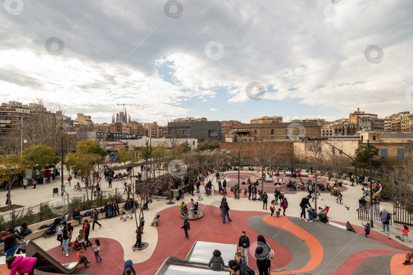 Скачать 03 МАРТА 2022 года, БАРСЕЛОНА, ИСПАНИЯ: Дети с родителями играют на детской площадке в центре города в пасмурный день фотосток Ozero