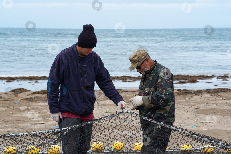 Скачать рыбаки проверяют и чинят рыболовную сеть на берегу фотосток Ozero