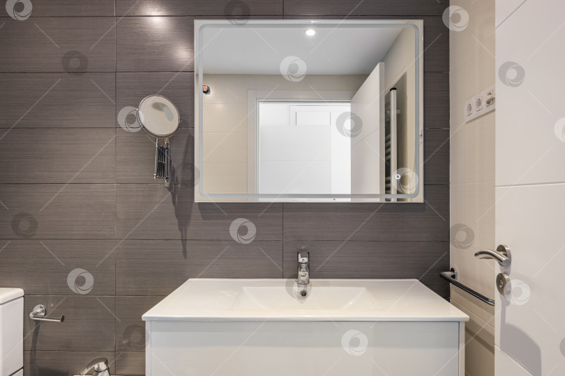 Скачать Современная ванная комната с серой плиткой, туалетом и прямоугольным большим зеркалом с подсветкой фотосток Ozero