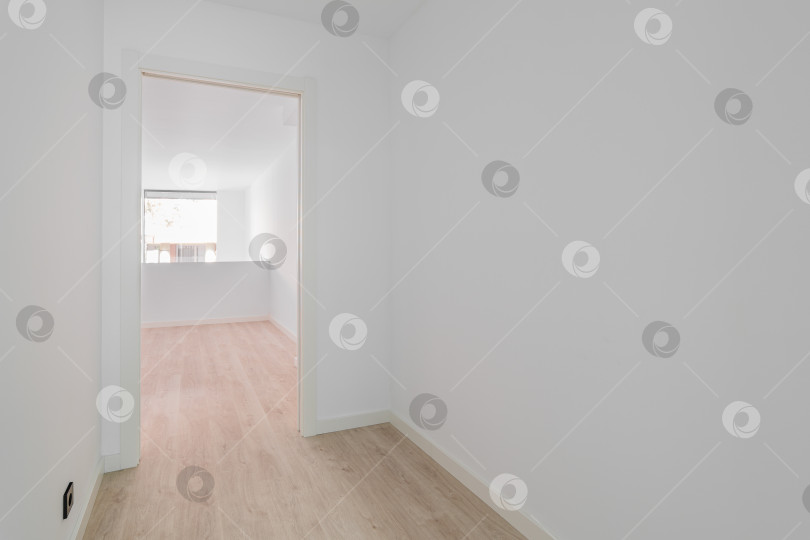 Скачать Пустая чистая комната после ремонта с белыми стенами, деревянным полом и дверью в другую комнату фотосток Ozero