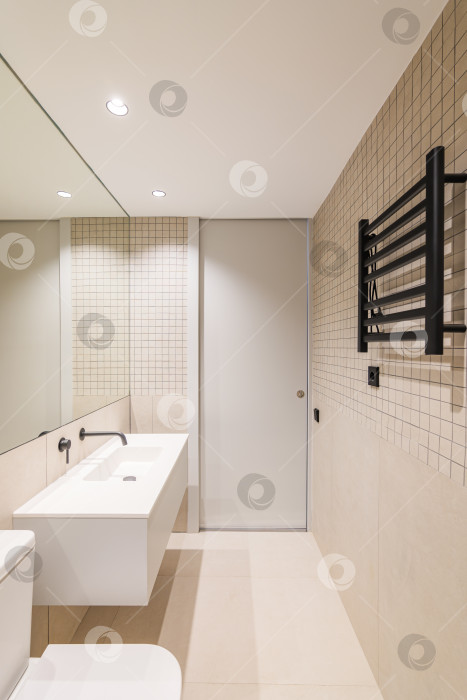 Скачать Вертикальный вид интерьера современной ванной комнаты с бежевой плиткой, черным радиатором и белой раковиной фотосток Ozero