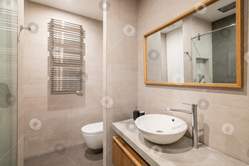 Скачать Интерьер современной ванной комнаты, выложенной плиткой, с белым унитазом, радиатором и душем в отражении зеркала в деревянной раме. фотосток Ozero