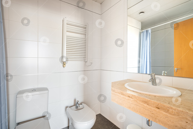 Скачать Интерьер ванной комнаты, выложенной белой плиткой, с туалетом, биде, радиатором и занавеской для душа в отражении зеркала фотосток Ozero