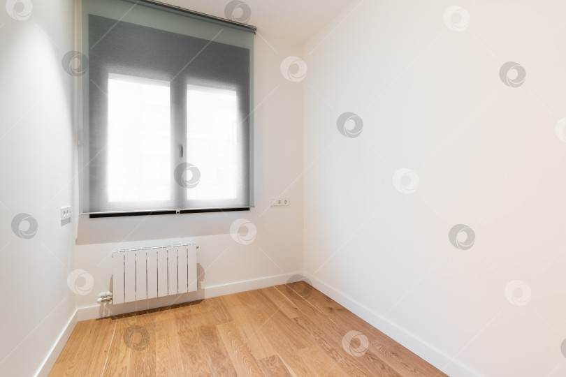 Скачать Пустая комната с ярким окном, ламинатным полом и недавно покрашенными в белый цвет стенами в отремонтированной квартире фотосток Ozero