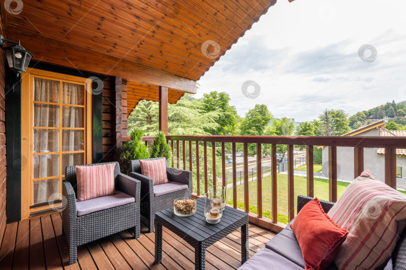Скачать Деревянный коттедж с красивой террасой и столом с креслами. Уютный и симпатичный дом в солнечный день в европейской деревне. фотосток Ozero