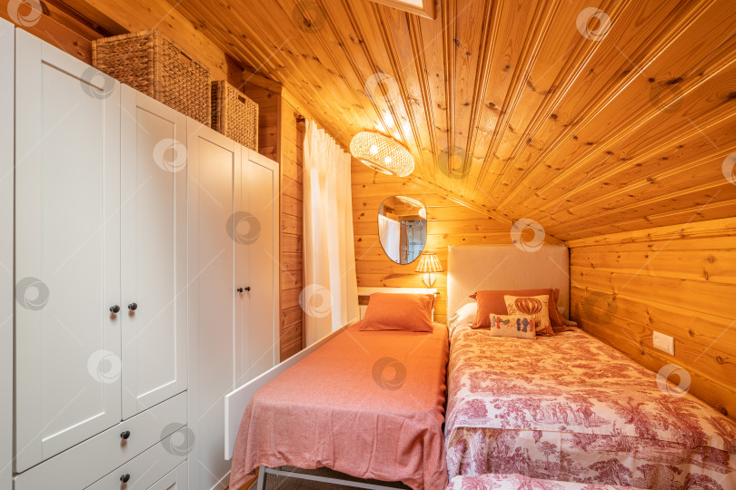 Скачать Небольшая спальня с двумя кроватями и белым шкафом в современном коттедже с деревянными стенами. фотосток Ozero