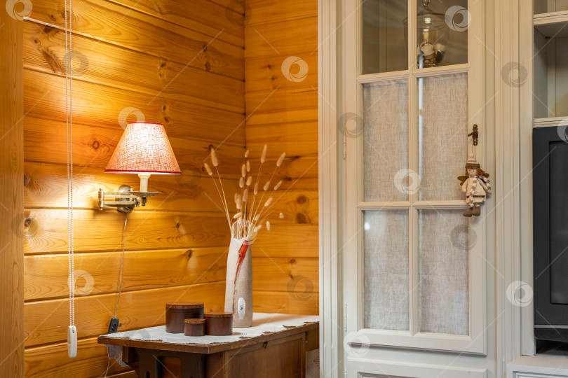 Скачать Уютный уголок с лампой, вазой с цветами и шкафом. Домашний декор в гостиной с деревянными стенами. фотосток Ozero