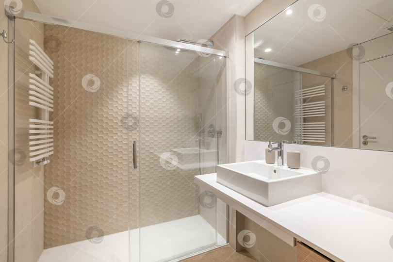 Скачать Просторный интерьер современной ванной комнаты, отделанной кафелем, с белой раковиной, большим зеркалом и душевой зоной. фотосток Ozero