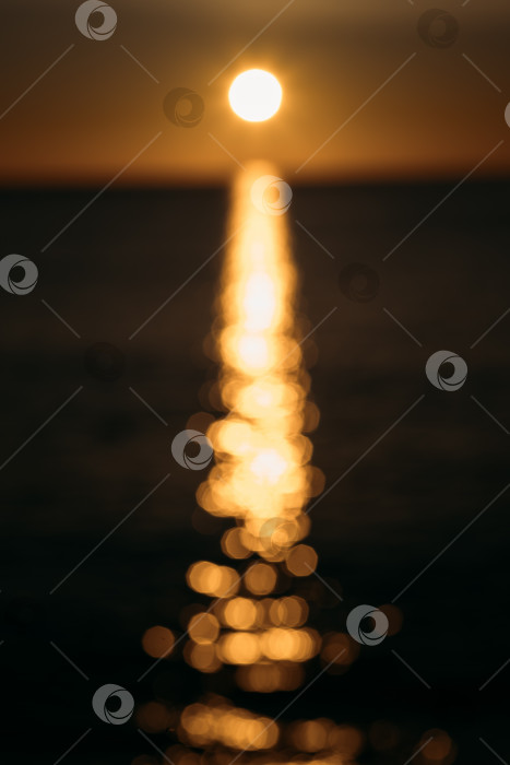 Скачать На размытом абстрактном фоне заката ярко-желтый солнечный диск отбрасывает блики на морскую воду. Великолепный золотистый размытый фон заката в наступающих тропических сумерках. фотосток Ozero