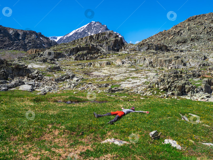 Скачать Человек лежит на природе и отдыхает. Счастливый турист мужского пола после восхождения лежит и отдыхает на зеленой траве на фоне гор. фотосток Ozero