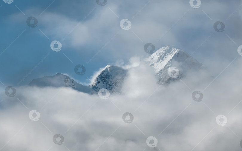 Скачать Мягкий фокус. Чудесный минималистский пейзаж с большими заснеженными горными вершинами над низкими облаками. Атмосферный минимализм с большими заснеженными горными вершинами, темным ледником на фоне впечатляющего неба. фотосток Ozero