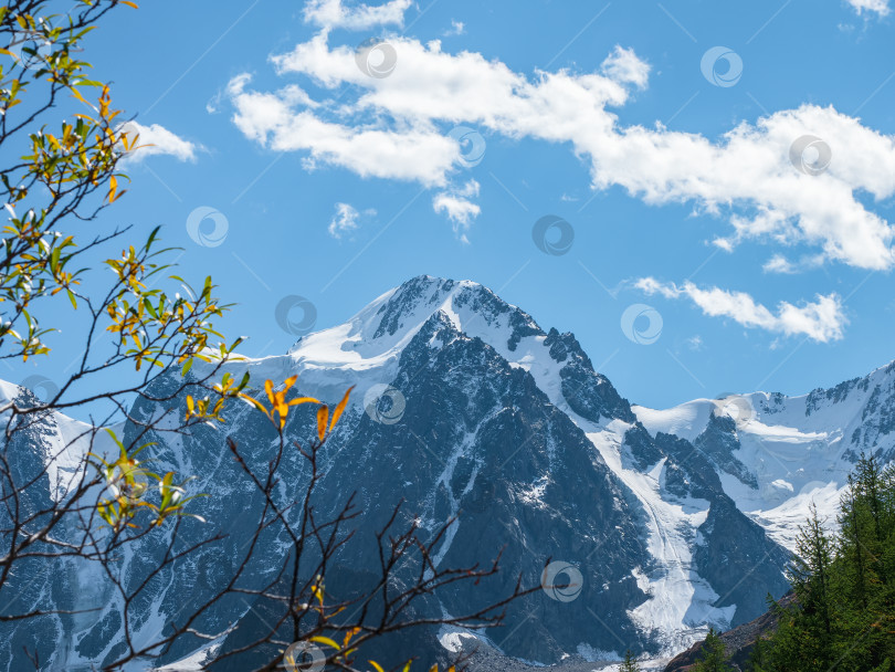 Скачать Белые облака над высокой остроконечной горой. Заснеженный высокогорный альпийский пейзаж с заснеженной горной вершиной и острыми скалами под облачным голубым небом. фотосток Ozero