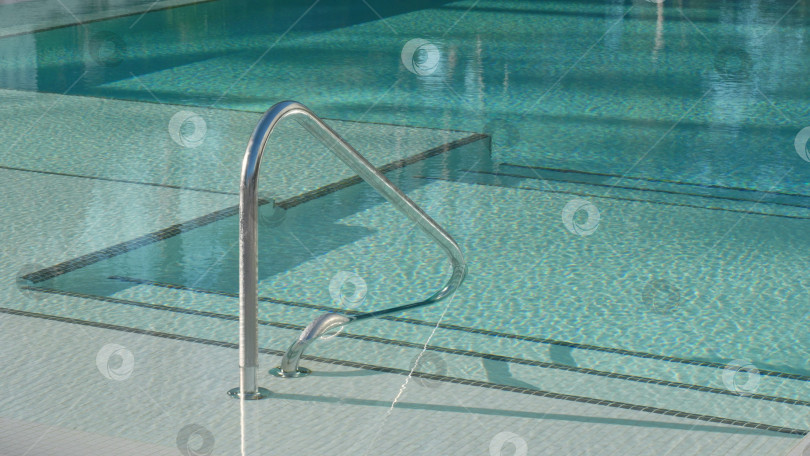 Скачать Спуск к бассейну с сине-бирюзовой водой и металлической лестницей. Отдохните на свежем воздухе в солнечный день. фотосток Ozero
