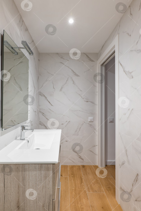 Скачать Ванная комната с белой плиткой, зеркалом, керамической раковиной под шкафом в современном доме или офисе. фотосток Ozero