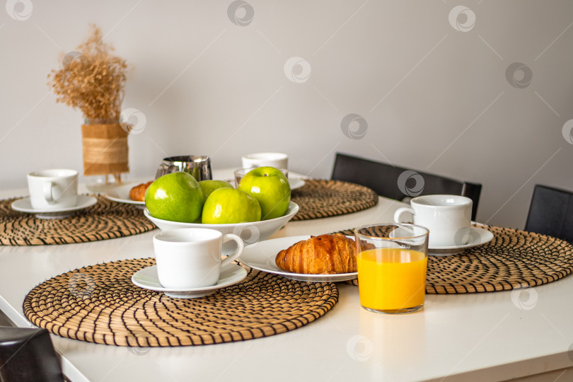 Скачать Свежий вкусный завтрак подается на белом столе с круассанами, яблоками и апельсиновым соком. фотосток Ozero