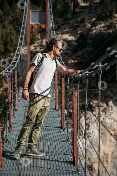 Скачать Турист стоит на подвесном мосту и смотрит вниз, на озеро. Концепция путешествия фотосток Ozero