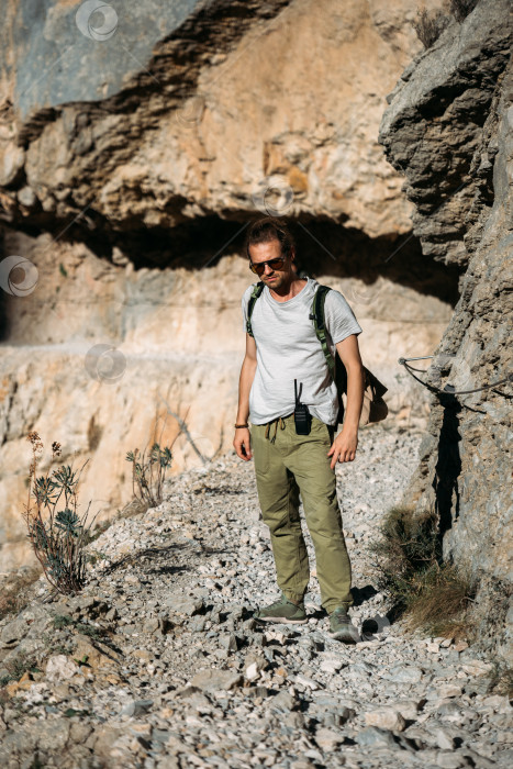 Скачать Брутальный путешественник-мужчина, отправляющийся в поход по горам с портативной рацией на открытом воздухе, на дикой природе. Турист с рюкзаком и рацией. фотосток Ozero