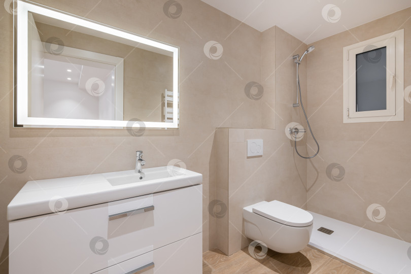 Скачать Современная ванная комната с бежевой плиткой, душем, туалетом и большим прямоугольным зеркалом с подсветкой фотосток Ozero