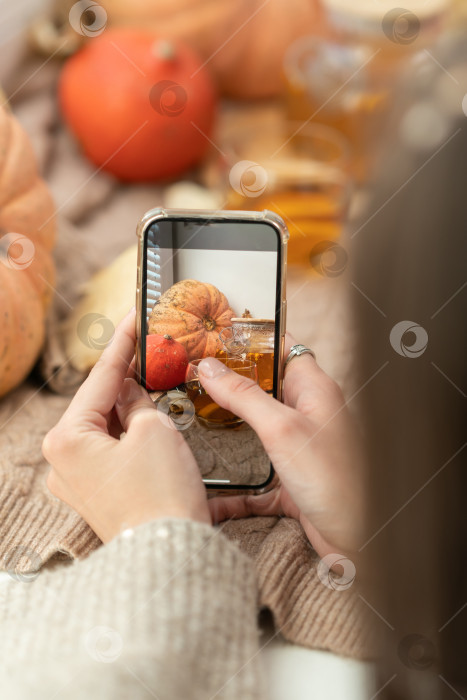 Скачать Девушка фотографирует тыквы, осенние листья и чайник на окне. Девушка фотографирует на телефон деревенскую композицию на Хэллоуин. Счастливого Дня благодарения и Хэллоуина фотосток Ozero