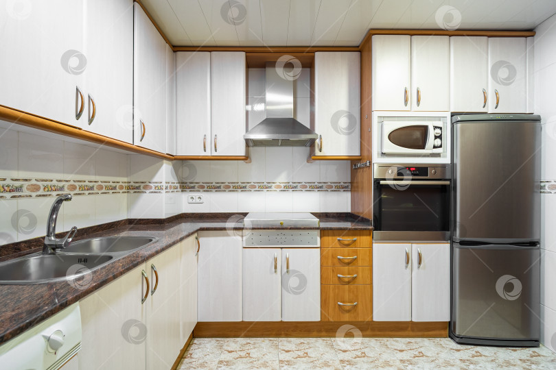 Скачать Пустая кухня в старом стиле со шкафчиками, выложенными плиткой стенами, мраморной столешницей и типичной бытовой техникой фотосток Ozero