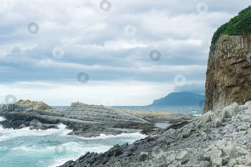 Скачать скалистый берег моря, образованный столбчатым базальтом на фоне штормового моря, прибрежный пейзаж Курильских островов фотосток Ozero